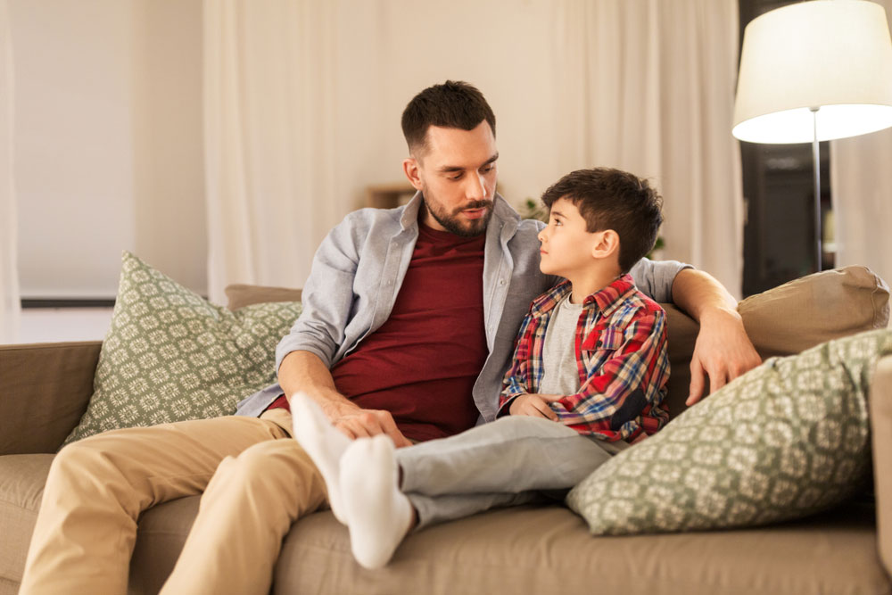 family, relationships and trust concept - father talking to his sad little son at home in evening