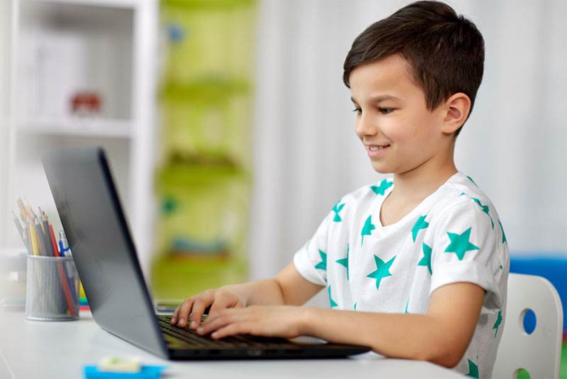 education, technology and people concept - smiling student boy typing on laptop computer a